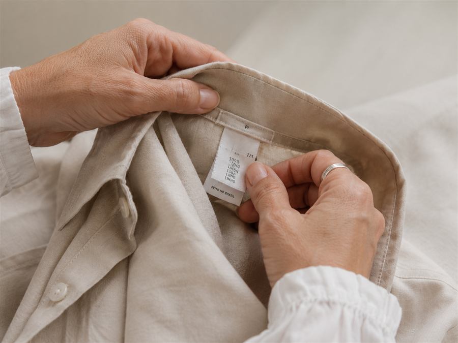 Mãos conferindo a etiqueta de composição de uma camisa de linho