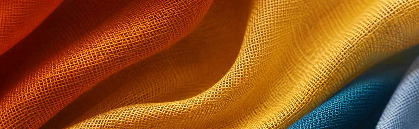 Close-up de tecidos sobrepostos em laranja, amarelo e azul, mostrando textura e queda do tecido.